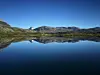 Fjellvannet Trollsjøen ligger speilblankt. Blå himmel.
