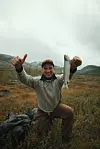 Sportsfisker med fanget fisk og tommel opp i et høstlig fjellandskap.