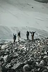 Fire fjellvandrere på en steinete rygg foran snødekte fjellsider.