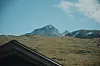 Åpent fjellandskap i Jotunheimen med en markant fjelltopp og et mørkt hustak i forgrunnen.