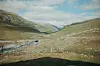 Steinete fjelldal med en bekk under en delvis skyet himmel.